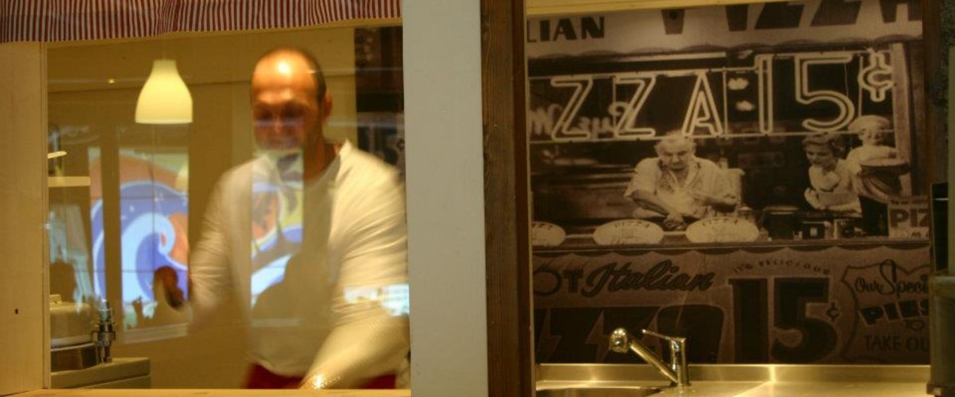 Uomo dietro vetro con immagine vintage di pizzeria, atmosfera retrò.