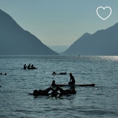 Persone rilassate su tavole da surf in un lago tra le montagne al tramonto.