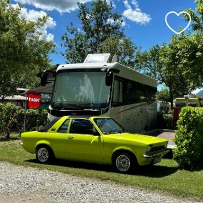 Auto gialla vintage parcheggiata davanti a un camper in un'area verde.