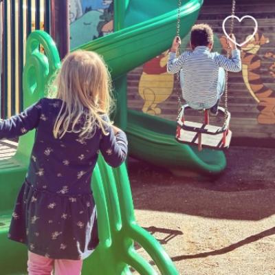 Bambini giocano al parco, uno sulla giostra e l'altro sullo scivolo verde.
