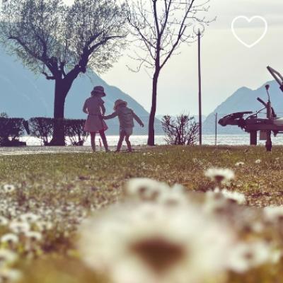 Due bambini giocano in un parco vicino a un lago, con montagne sullo sfondo.