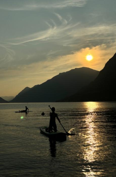 Tramonto colorato sul lago con persone e camper in silhouette.