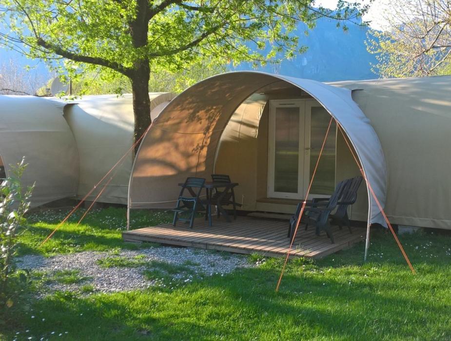 Tenda glamping moderna con veranda e sedie su prato verde in campeggio.