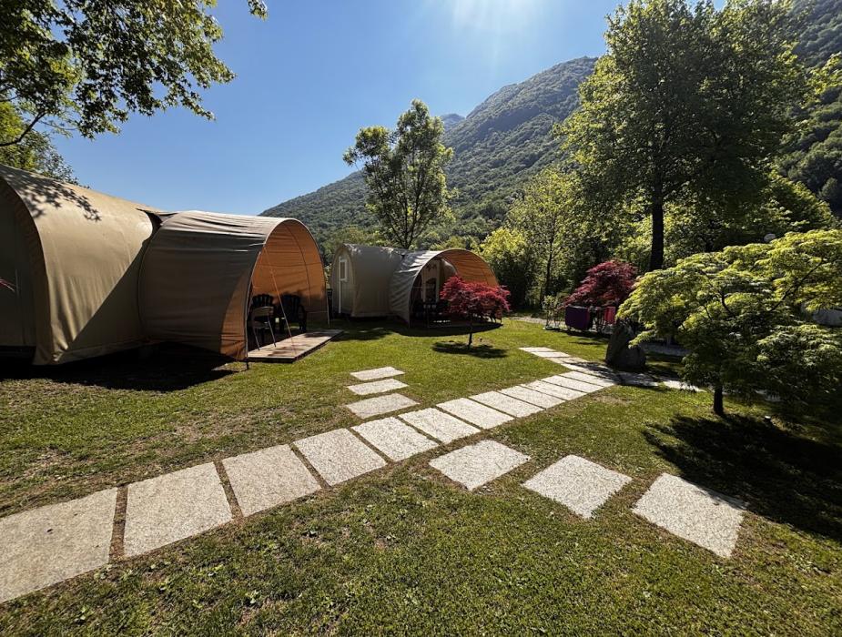 Tenda glamping con veranda e sedie, immersa in un verde paesaggio collinare.