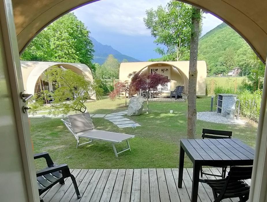 Campeggio con bungalow e auto, circondato da montagne e verde.