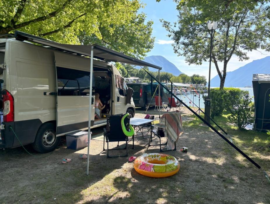 Auto verde accanto a un camper in un'area verde con alberi.