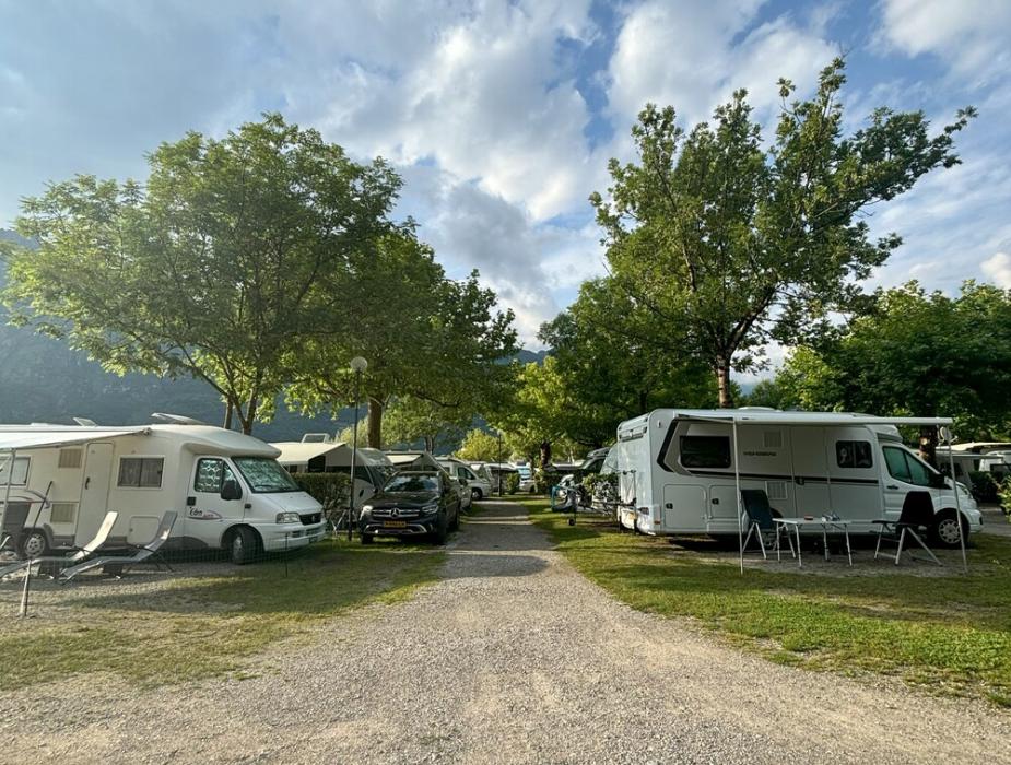 Campeggio con camper e roulotte sotto un cielo nuvoloso e alberi verdi.