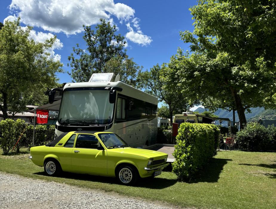Auto gialla e camper in un campeggio verde sotto un cielo sereno.