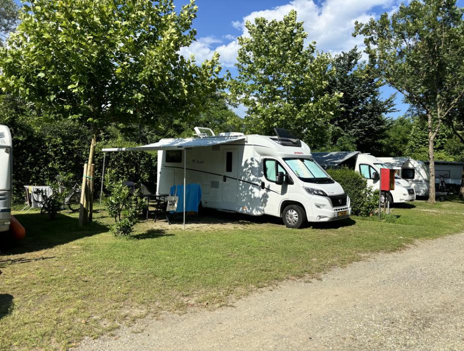 Camper in campeggio sotto gli alberi con tende da sole aperte.
