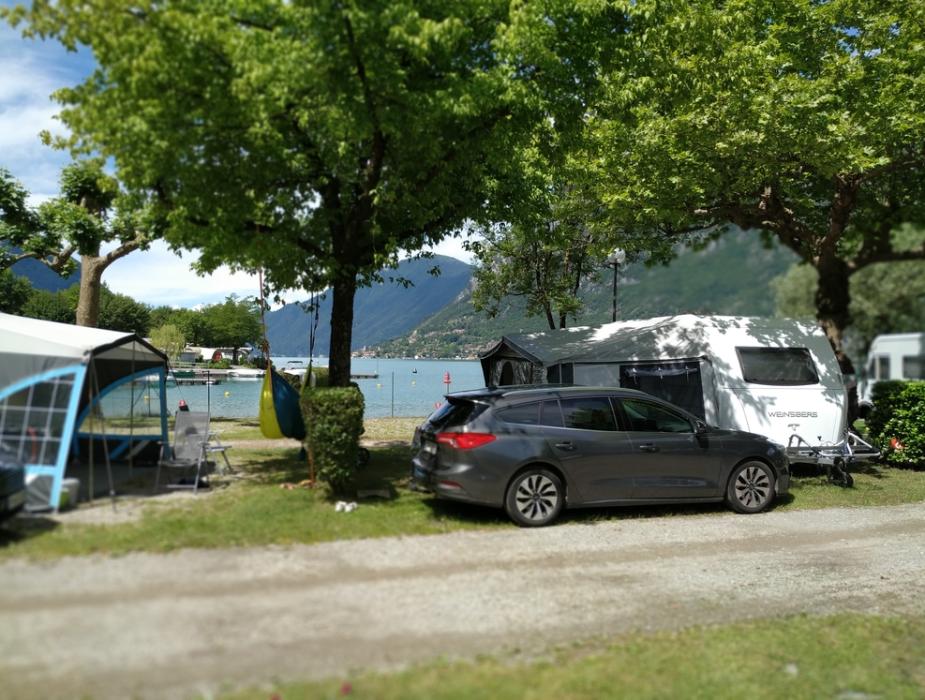 Campeggio sul lago con roulotte, auto e amaca sotto gli alberi.