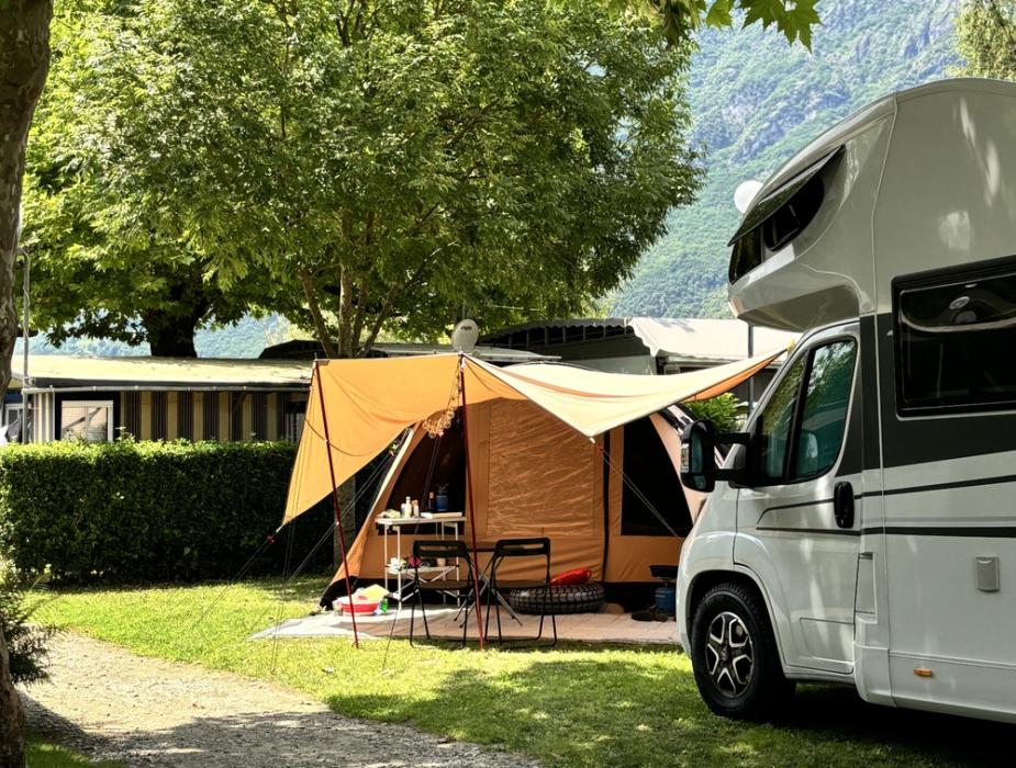 Campeggio con tenda e camper sotto gli alberi, in un ambiente montano.