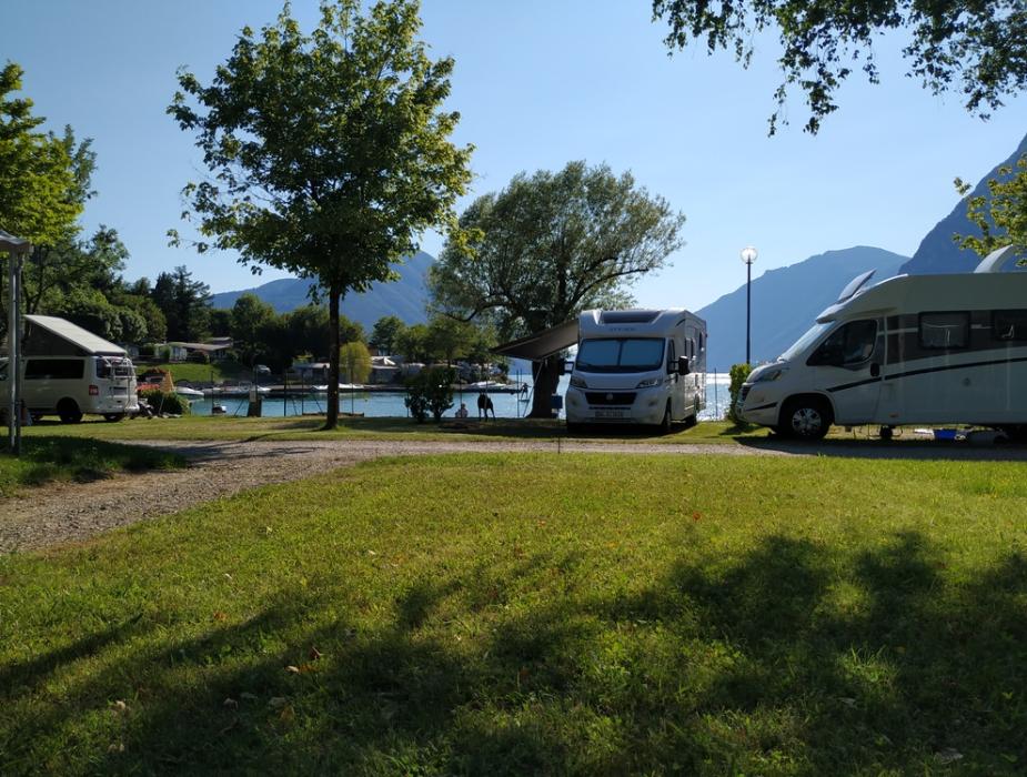 Camper parcheggiati vicino a un lago, circondati da alberi e montagne.