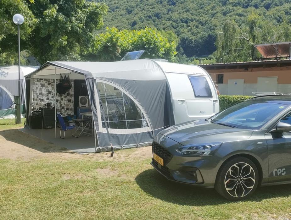Camper con veranda e auto parcheggiata, immersi nella natura con alberi verdi.