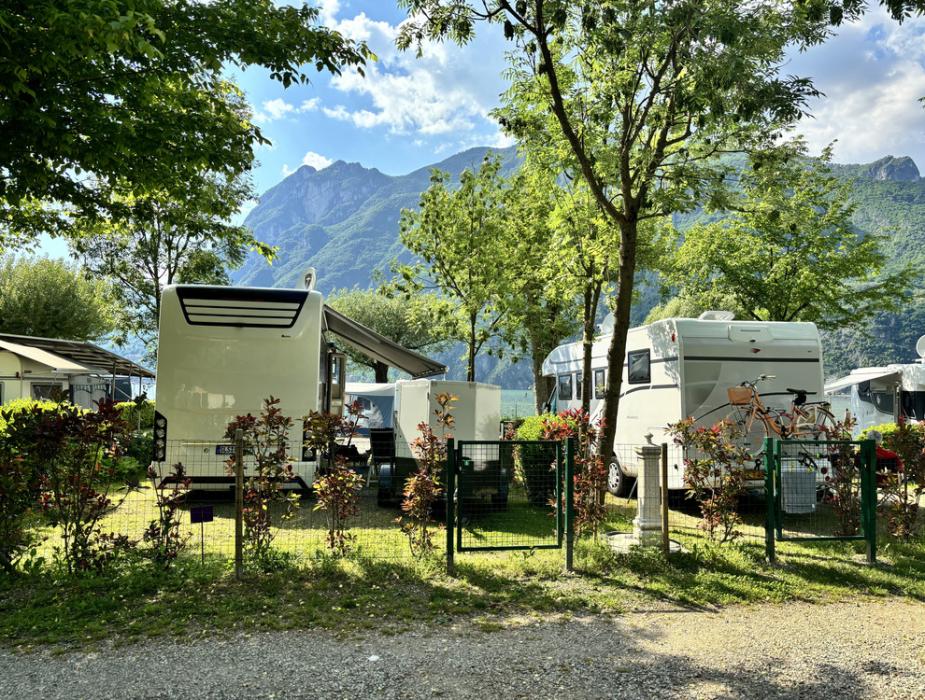 Camper parcheggiati in un campeggio con vista sulle montagne e alberi verdi.