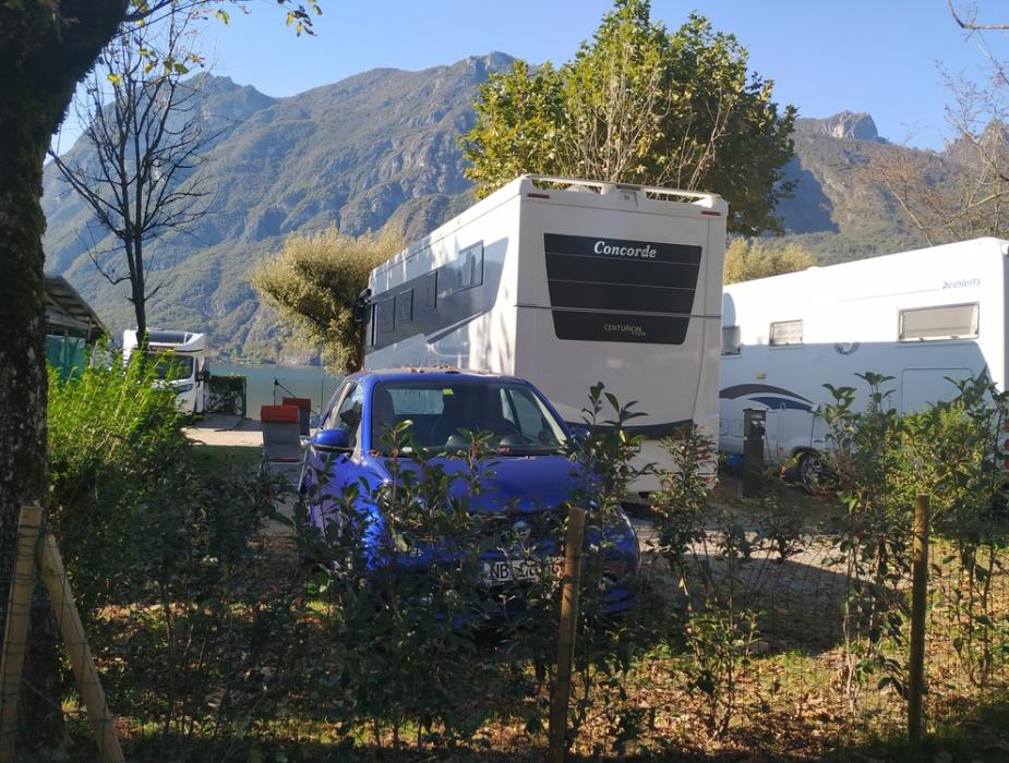 Camper e auto in campeggio, montagne sullo sfondo, giornata soleggiata.