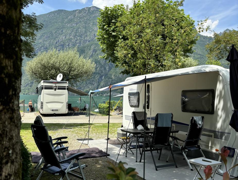 Camper in campeggio con vista montagna, sedie e tavolo all'aperto.