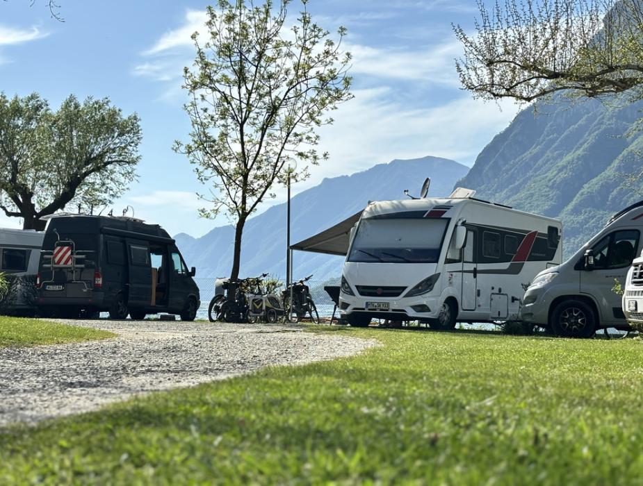Camper parcheggiati vicino a un lago, circondati da montagne e alberi.