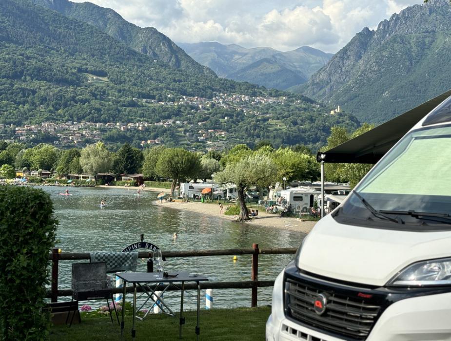 Campeggio sul lago con vista su montagne e camper parcheggiato.
