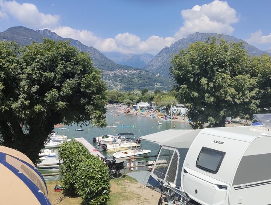 Campeggio sul lago con roulotte, tenda e montagne sullo sfondo.