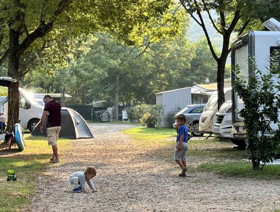 Famiglia in campeggio con bambini che giocano su un sentiero alberato.