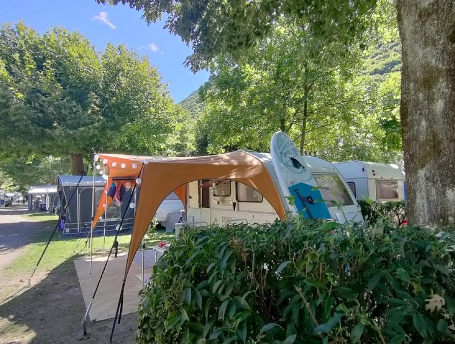 Campeggio con roulotte e tenda sotto alberi verdi in una giornata soleggiata.