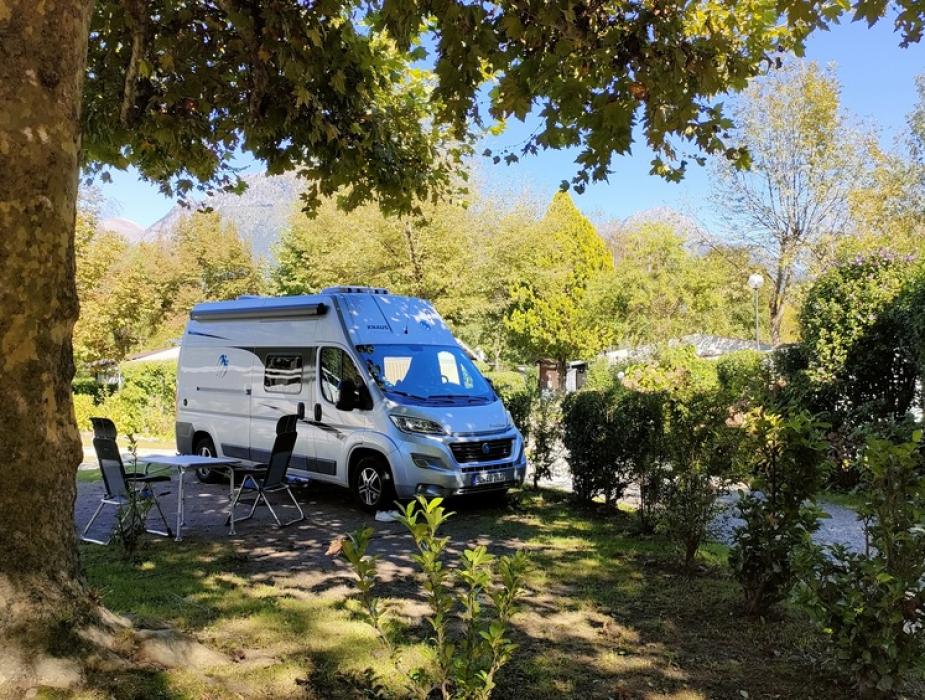 Camper parcheggiato in un'area verde con tavolo e sedie sotto un albero.