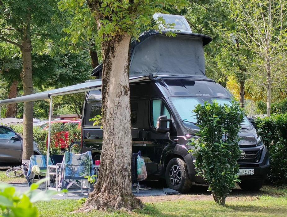 Camper nero con tettuccio aperto, sedie e tavolo in un'area verde.