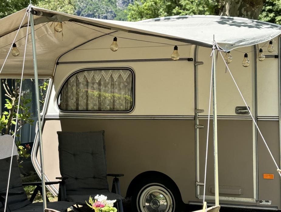 Caravan vintage con tenda, sedie e luci, immerso nella natura.