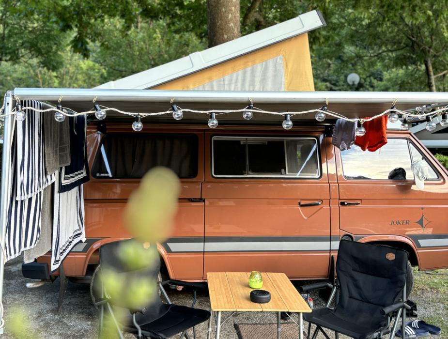 Camper vintage con tenda, sedie e tavolo da campeggio sotto un albero.
