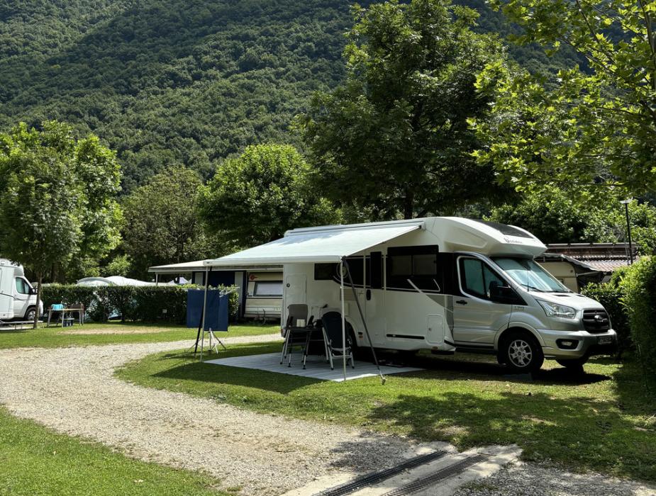 Camper parcheggiato in un'area verde con montagne e cielo sereno sullo sfondo.