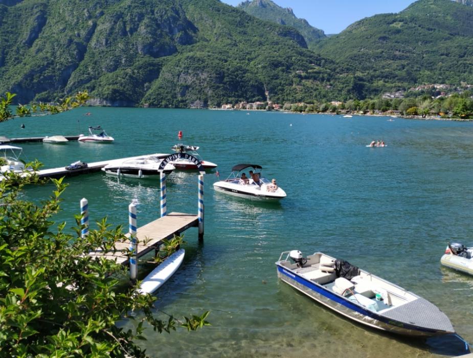 Barche ormeggiate su un lago circondato da montagne verdi e paesaggio naturale.