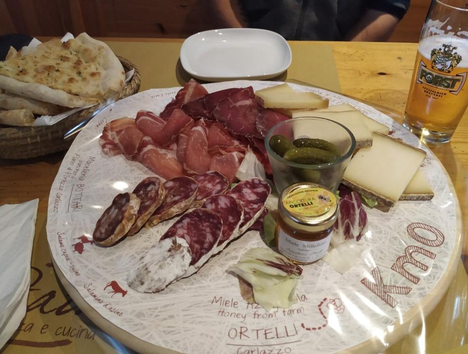 Tagliere di salumi e formaggi con miele e cetriolini, accompagnato da birra e focaccia.