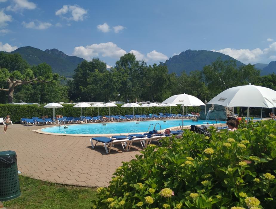 Piscina all'aperto con lettini, ombrelloni e vista sulle montagne.