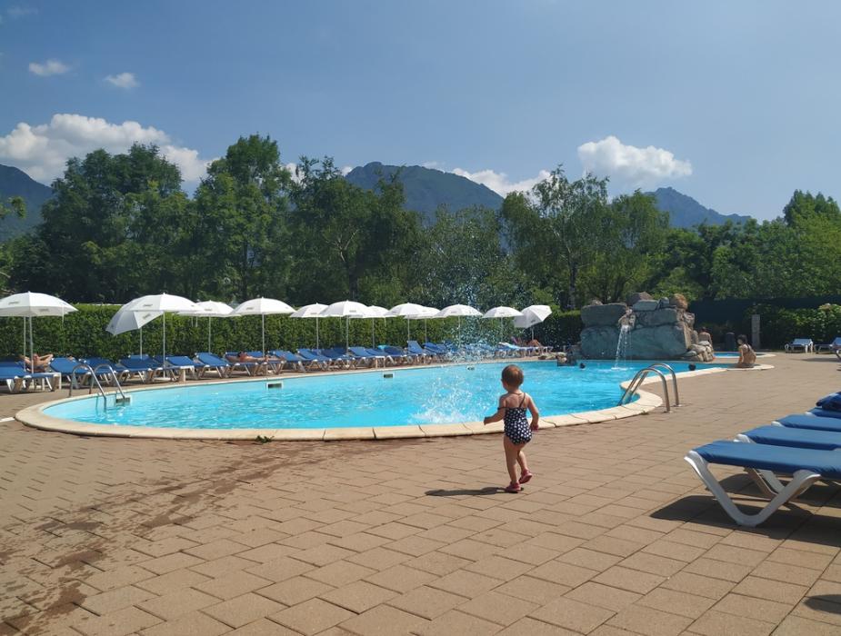 Bambina cammina vicino a una piscina all'aperto con lettini e ombrelloni.