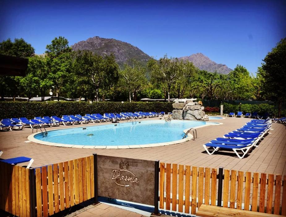 Piscina all'aperto circondata da lettini blu e vista montagna.