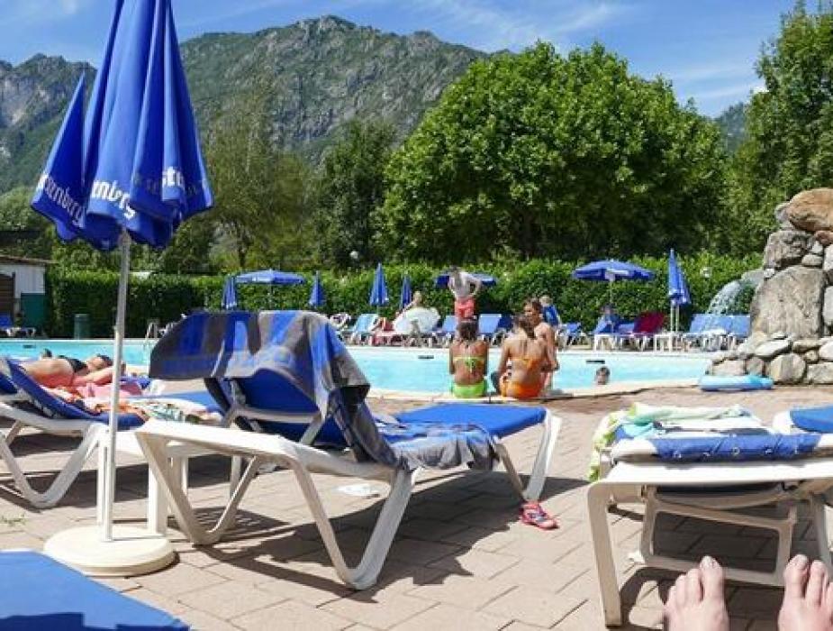 Piscina all'aperto con lettini blu, ombrelloni e vista sulle montagne.