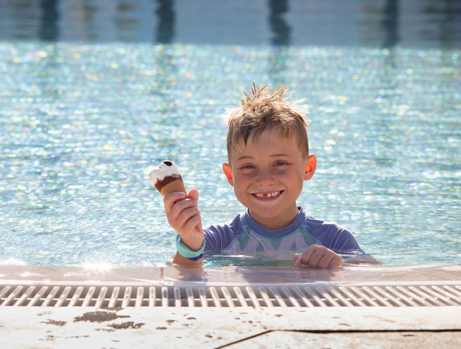Bambino felice in piscina con gelato in mano, sotto il sole.