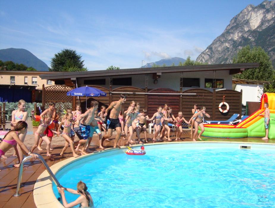 Gruppo di bambini e adulti pronti a tuffarsi in piscina all'aperto.