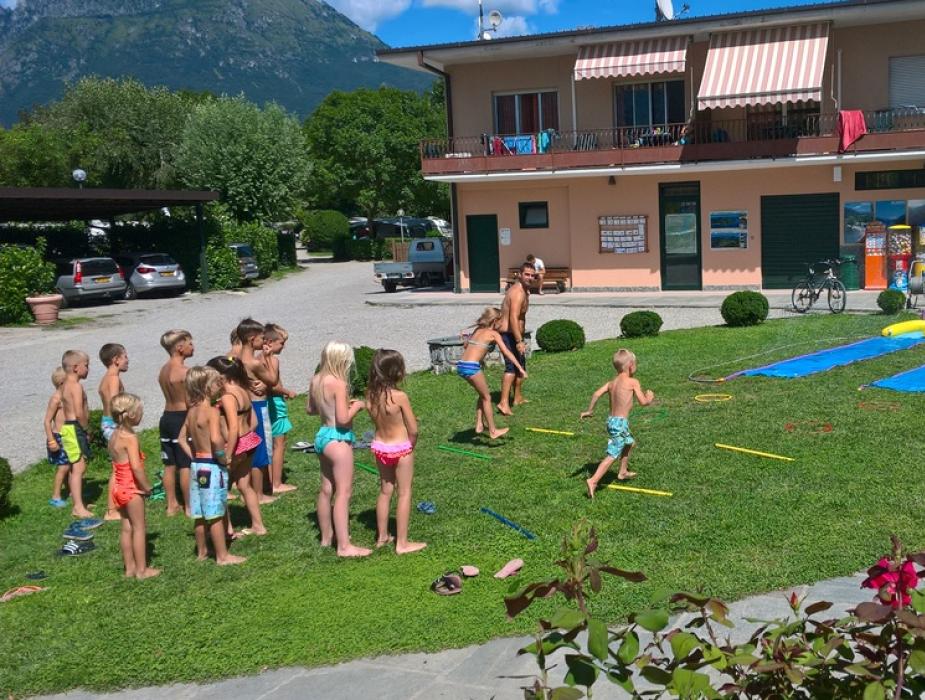 Bambini giocano all'aperto su tappetini scivolosi in un cortile soleggiato.
