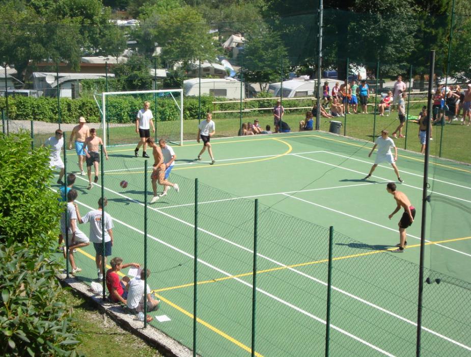 Partita di calcetto all'aperto con spettatori su un campo verde.