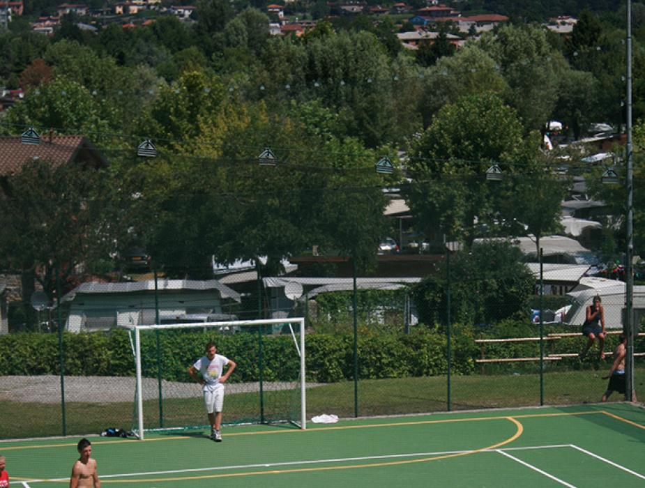 Partita di calcetto all'aperto con giocatori in azione su campo verde.