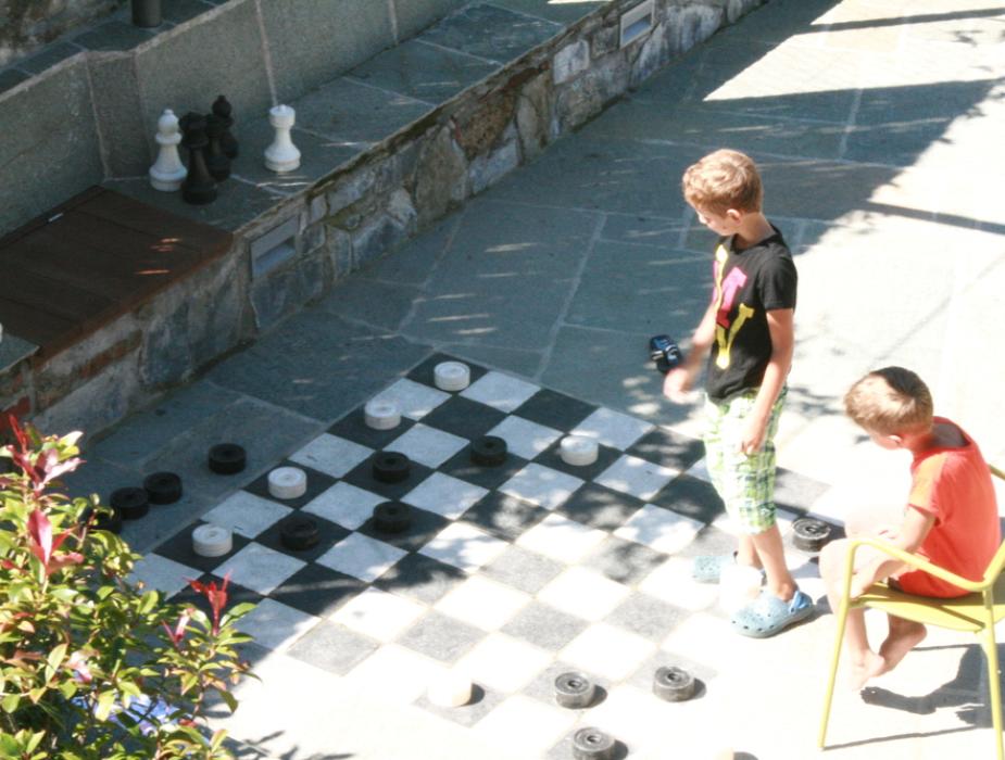 Due bambini giocano a dama gigante all'aperto su una scacchiera pavimentata.
