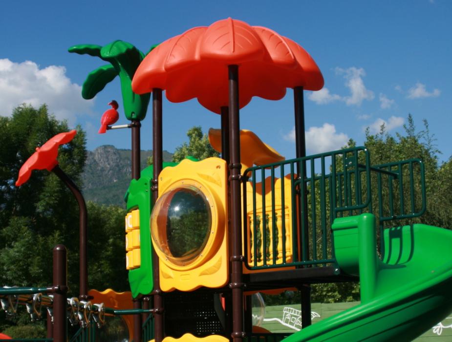 Parco giochi colorato con scivolo verde e strutture a tema natura.