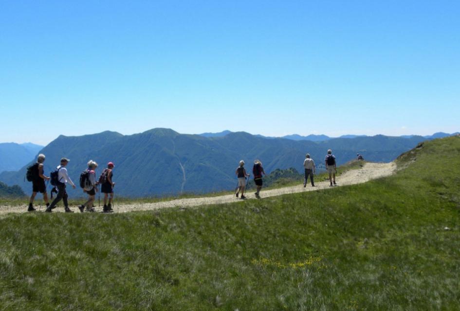 Escursionista ammira il panorama montano con lago, cielo sereno e montagne all'orizzonte.